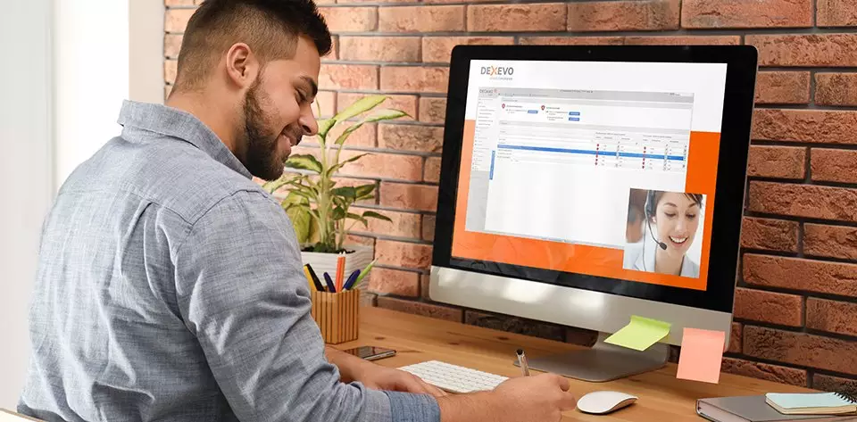 Mann am Schreibtisch mit einem PC-Monitor, wo ein DEXEVO-Mitarbeiter die DECAMS DEMO erklärt und zeigt